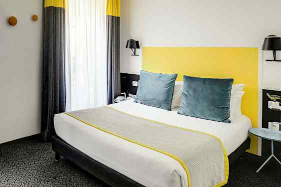 Ett hotellrum med en säng utrustad med grå och gula detaljer. (AI-genererad text)