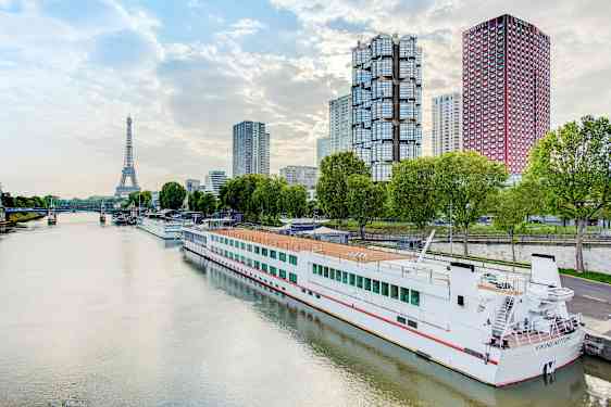 Flod med en båt vid kaj, moderna byggnader och Eiffeltornet i bakgrunden. (AI-genererad text)