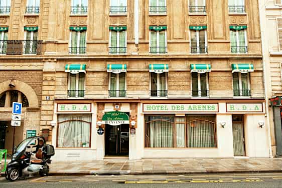 Byggnad med hotellfasad, skyltar med texten 'Hotel des Arenes' och grönvita markiser ovanför fönstren. (AI-genererad text)
