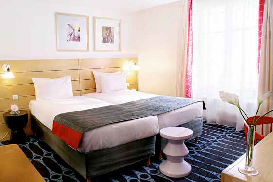 Ett hotellrum med två enkelsängar, en dekorativt inredd sänggavel och ett fönster med ljusinsläpp. (AI-genererad text)