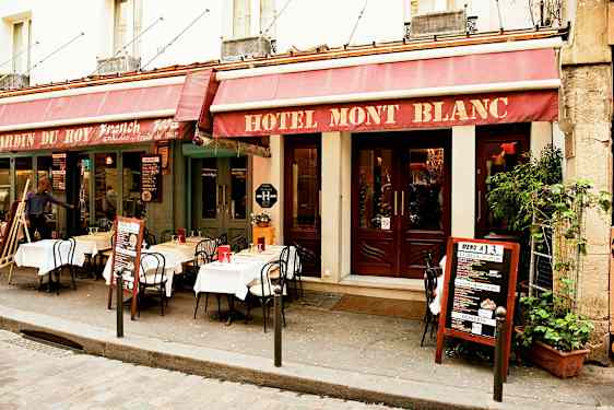 Utanför en hotellbyggnad med restaurang där bord och stolar är uppställda på trottoaren. (AI-genererad text)