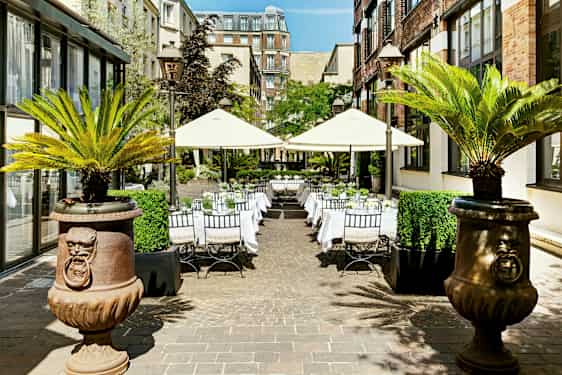 Utomhus sällskapsområde med bord och parasoller omgiven av byggnader och palmer. (AI-genererad text)