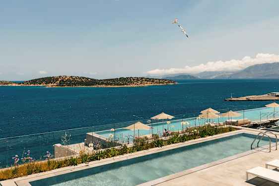 Bild av en infinitypool med utsikt över havet och omgivande öar. En glasbalustrad omger poolområdet, och parasoller finns vid poolkanten. (AI-genererad text)