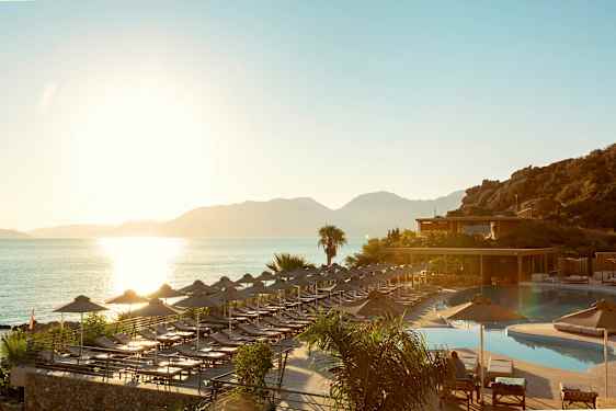 Solnedgång vid havet där solstolar och parasoller står vid en pool och en terrass. (AI-genererad text)