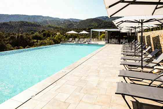 En infinitypool med solstolar och parasoller bredvid, belägen med utsikt över ett naturskönt bergslandskap. (AI-genererad text)