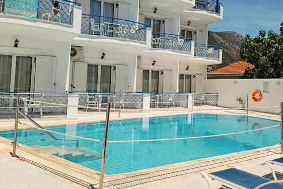 Bild av en pool framför ett vitmålat hotell med blåa balkonger och solstolar vid poolen. (AI-genererad text)