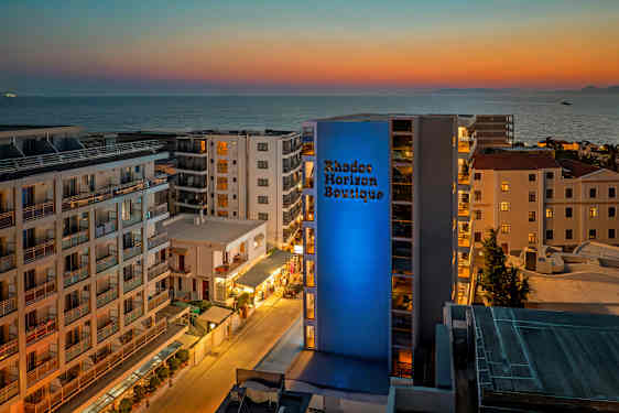 Vy över ett hotellområde med havet i bakgrunden vid solnedgången. (AI-genererad text)