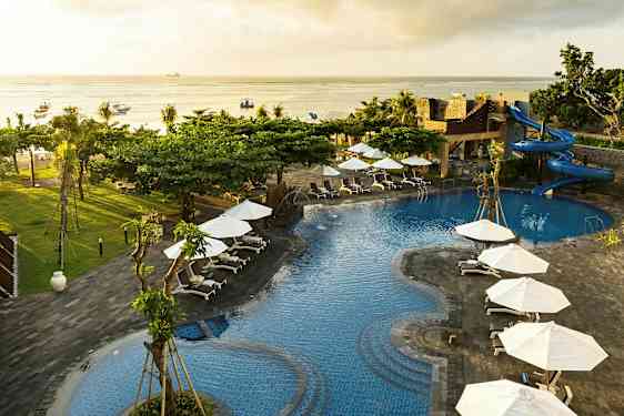 Bilden visar en poolområde med blå vatten, omgivna av solstolar och vita parasoller. Det finns en vattenrutschkana och utsikt över havet. (AI-genererad text)