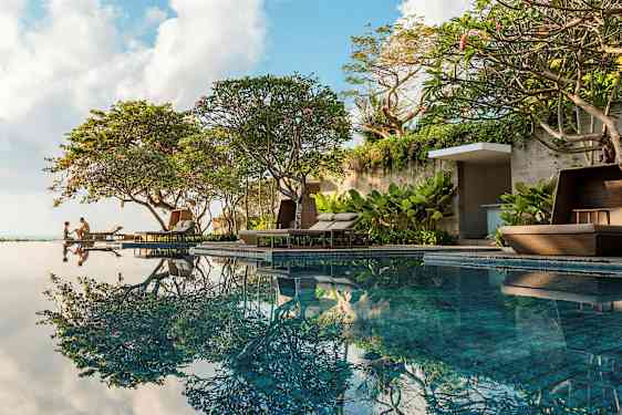 Pool nära grönskande träd och bekväma solstolar. (AI-genererad text)