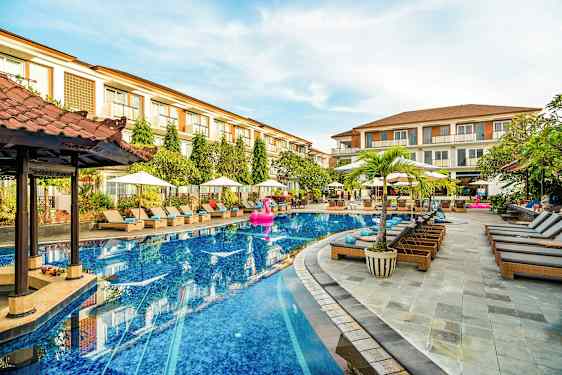 En hotellpool med solsängar och parasoller runt omkring, samt ett par byggnader i bakgrunden. (AI-genererad text)