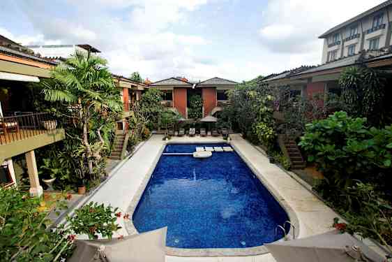 En utomhuspool omgiven av växter och byggnader. (AI-genererad text)