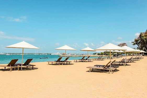 Strand med solstolar under parasoller vid havet. (AI-genererad text)