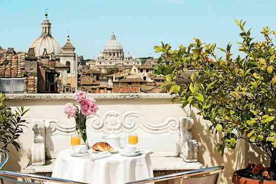 En terrass med ett bord dukat för frukost och utsikt över stadens tak och en katedral. (AI-genererad text)