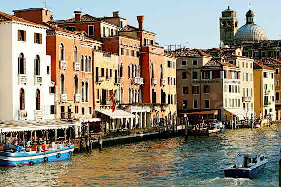 En bild av en kanal i Venedig med färgglada byggnader, båtar och en kupolformig kyrka i bakgrunden. (AI-genererad text)