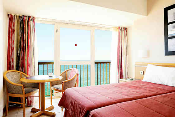 Ett hotellrum med två bäddar, ett litet bord och två stolar, samt en balkong med utsikt över havet. (AI-genererad text)