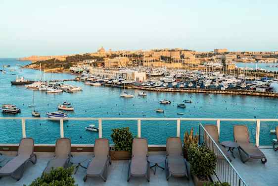 Vy över en marina med båtar och en terrass med solstolar. (AI-genererad text)