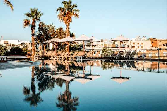 En pool med parasoller och solstolar på en solig dag. (AI-genererad text)