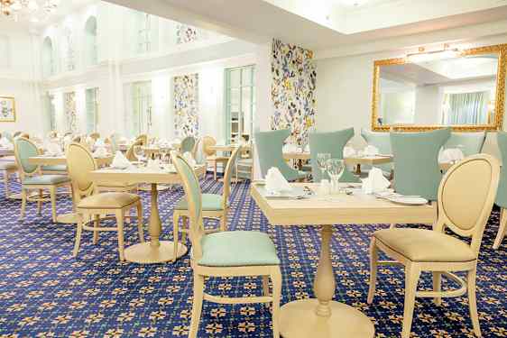 Ett ljust och elegant inrett matsalsutrymme med dukade bord och stolar, omslutet av väggar med mönstrade tapeter. (AI-genererad text)