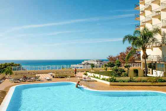 En utomhuspool med stallplatser och en klarblå himmel över havet. (AI-genererad text)