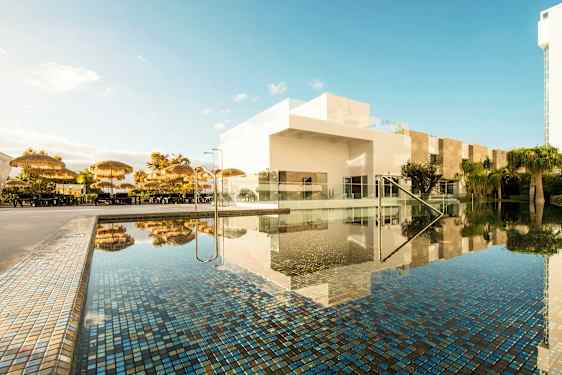 Poolområde med parasoller och vita byggnader. (AI-genererad text)