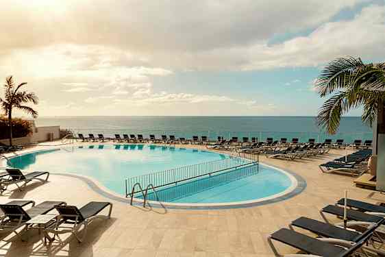 Utomhuspool med solsängar runt omkring, belägen nära havet under en klar himmel. (AI-genererad text)