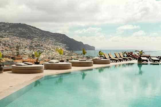 En infinitypool med solstolar och utsikt över en stad och berg. (AI-genererad text)