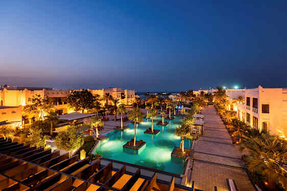 En upplyst semesterort med pooler och palmer på kvällen. (AI-genererad text)