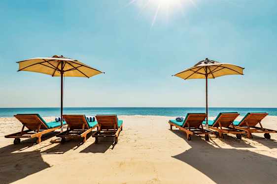 Strandstolar med parasoller på en sandstrand, med havet i bakgrunden. (AI-genererad text)