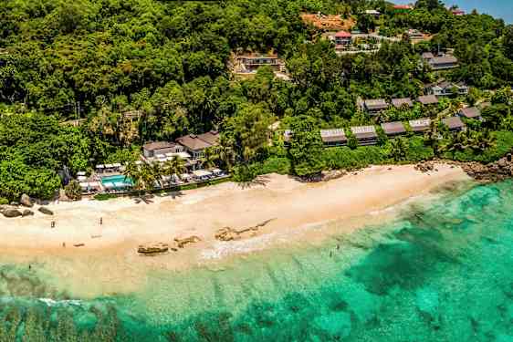 Strand med turkost vatten, omgiven av lummig vegetation och byggnader. (AI-genererad text)