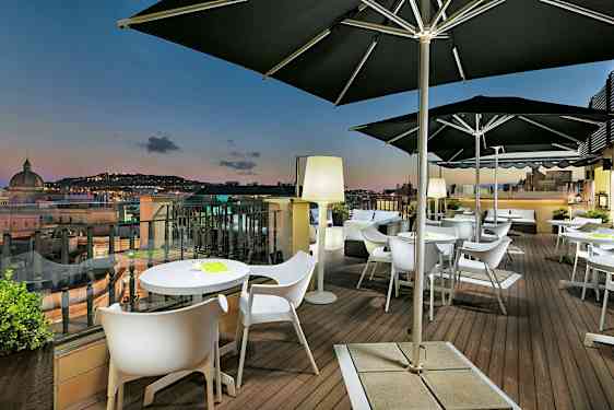 En terrass med bord och stolar, samt utsikt över en stad i skymningsljus. (AI-genererad text)