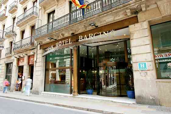 Ett hotell med en glasentré och dekorativ skylt ovanför, beläget vid en gata med trottoar. (AI-genererad text)