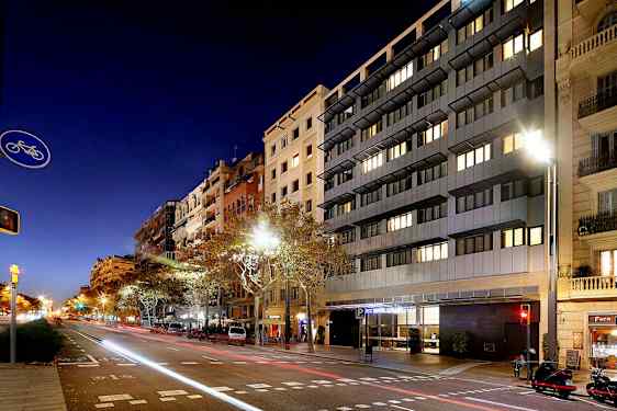 En gata i stadsmiljö på natten, med höga byggnader och bilar längs vägen. (AI-genererad text)