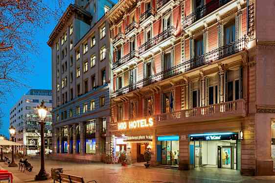 En stadsgata vid skymning med upplysta byggnader. En hotellskylt lyser starkt på fasaden. (AI-genererad text)