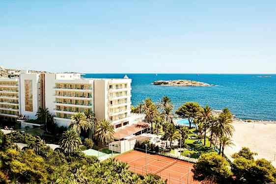 Bild av en semesteranläggning intill stranden med en byggnad, palmträd, pool och tennisbanor, belägen vid havet. (AI-genererad text)