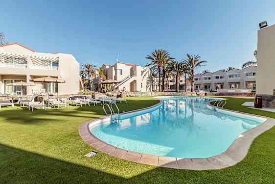 En utomhuspool omgiven av vita byggnader och solstolar på gräs. (AI-genererad text)