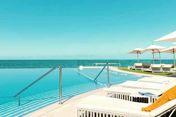 En infinitypool med utsikt över havet, omgiven av solstolar och parasoller. (AI-genererad text)