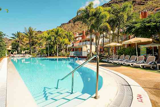 Utomhuspool med solsängar vid ett hotell, omgiven av palmer och gröna växter. (AI-genererad text)