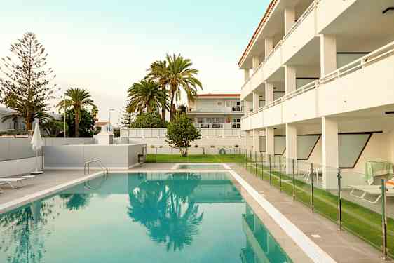 Utomhuspool med staket och omgivande byggnader i bakgrunden. (AI-genererad text)