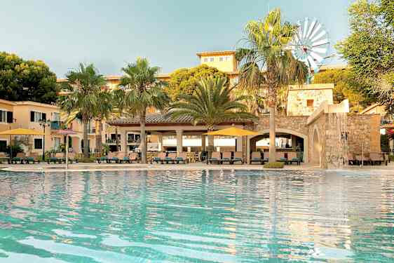 En pool framför en byggnad med palmer och en liten vindmölla synliga. (AI-genererad text)