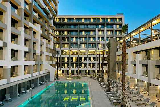 En modern hotellbyggnad med balkonger och en upplyst pool omgiven av solstolar. (AI-genererad text)