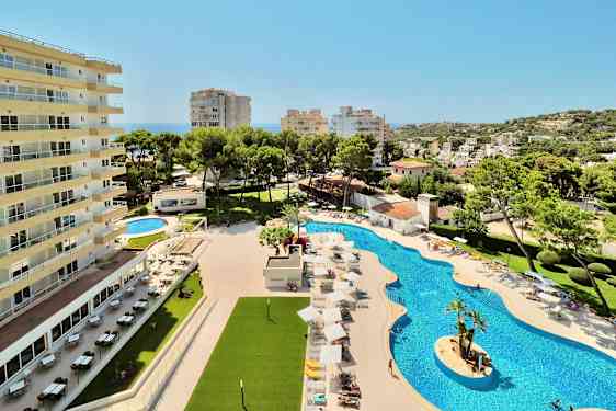 En hotellbyggnad bredvid en pool med solstolar och parasoller samt omgivande vegetation och utsikt över en stad. (AI-genererad text)