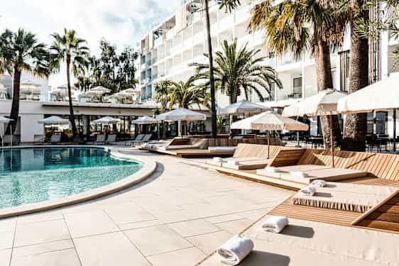 En pool omgiven av solstolar och parasoller vid ett hotell, med palmer i bakgrunden. (AI-genererad text)