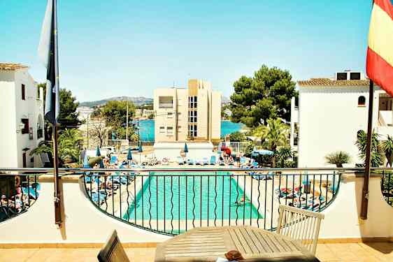 En pool med solstolar runtom och byggnader samt träd i bakgrunden. (AI-genererad text)