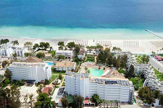 Flygbild över ett hotellområde nära stranden med parasoller på sanden och en klarblå havsvy. (AI-genererad text)