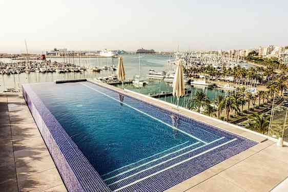 Bild på en infinitypool med utsikt över en småbåtshamn med palmer och flervåningsbyggnader i bakgrunden. (AI-genererad text)