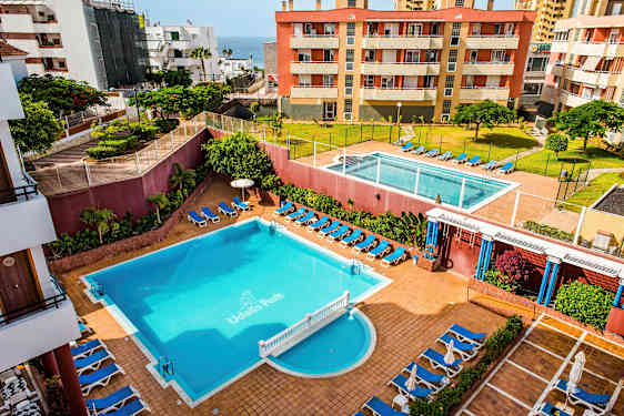 Ett hotellområde med två pooler, solsängar och omgivande byggnader. (AI-genererad text)