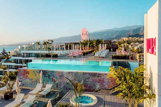 En stor takterrass med en pool, solstolar och växter. I bakgrunden berg och byggnader. (AI-genererad text)