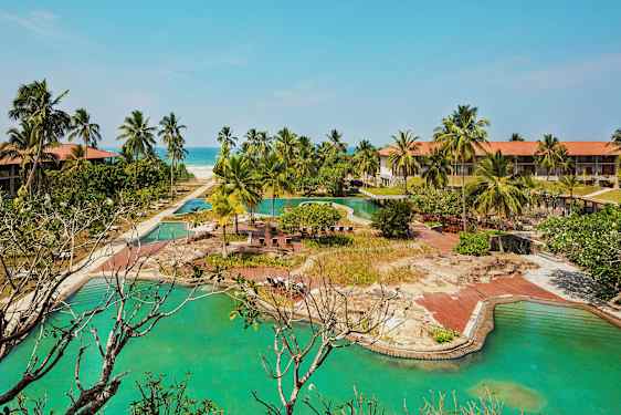 Hotellanläggning med pooler, palmer och en sandstrand i bakgrunden. (AI-genererad text)