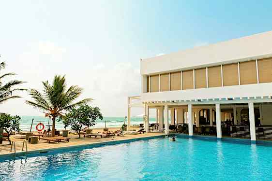 En utomhuspool med solstolar och palmer vid sidan av ett modernt hotell med utsikt över havet. (AI-genererad text)