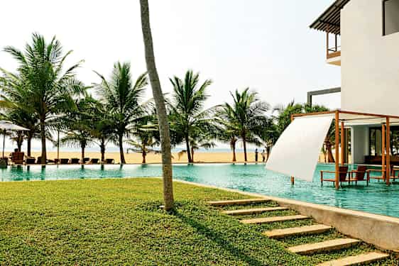 En pool vid havet med palmer i bakgrunden och en gräsmatta i förgrunden. (AI-genererad text)